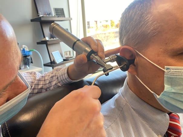 Dr. Richard Luekenga, Au.D. looking into patients ear with an otoscope during impacted earwax removal